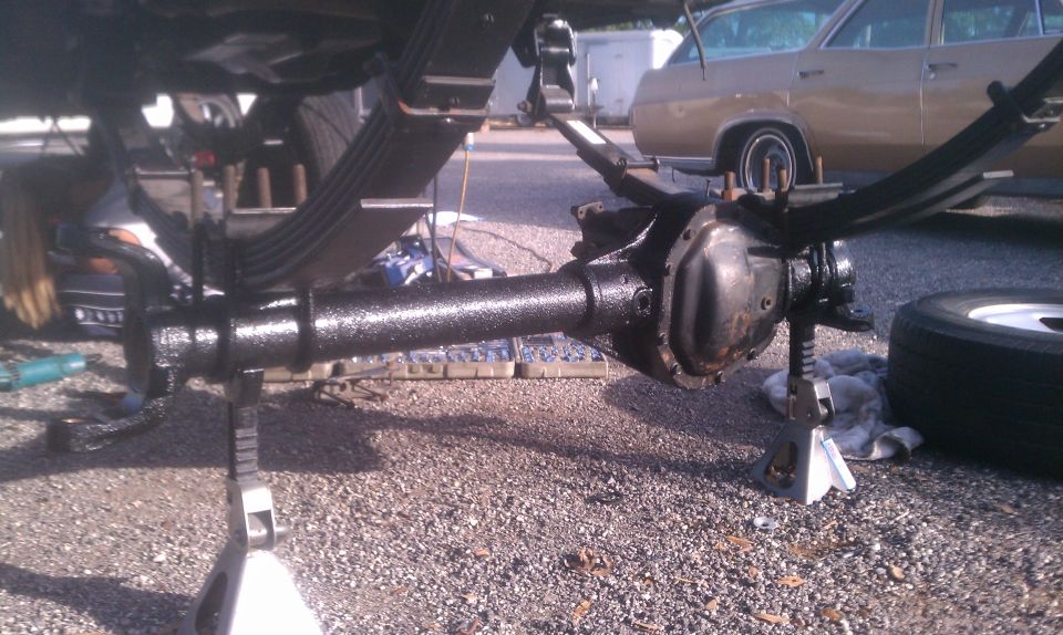rear axle assembly on jack stands, leaf springs visible, another vehicle in background