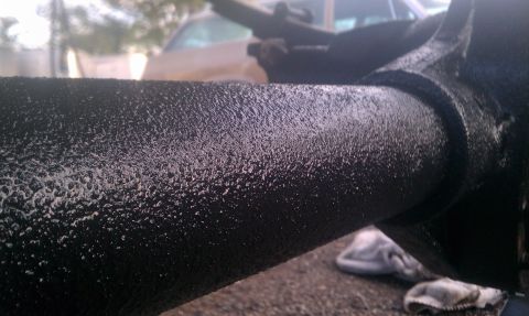 1995 Ford Bronco - Close-up of a black textured metal pipe and suspension component with a blurry vehicle in the background.
