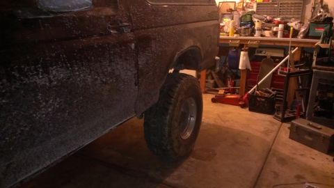 1995 Ford Bronco - Side view of a Ford Bronco's rear quarter panel and tire, seen in a cluttered garage.