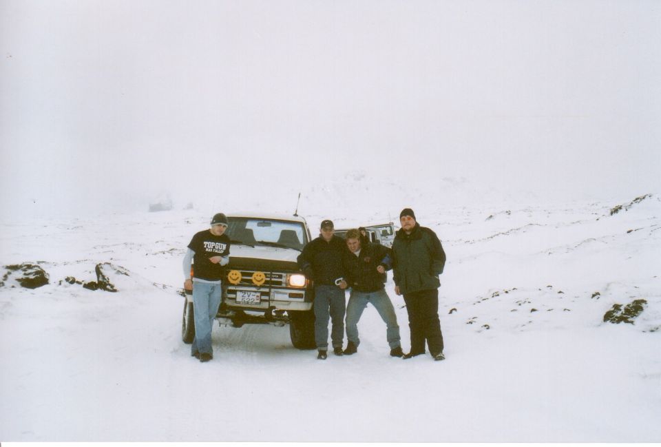 Four men posing in front of a white SUV with smiley stickers in snow