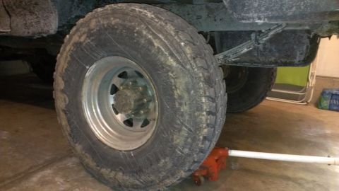 1995 Ford Bronco - The rear tire and suspension components of a vehicle are shown, with a jack supporting it.