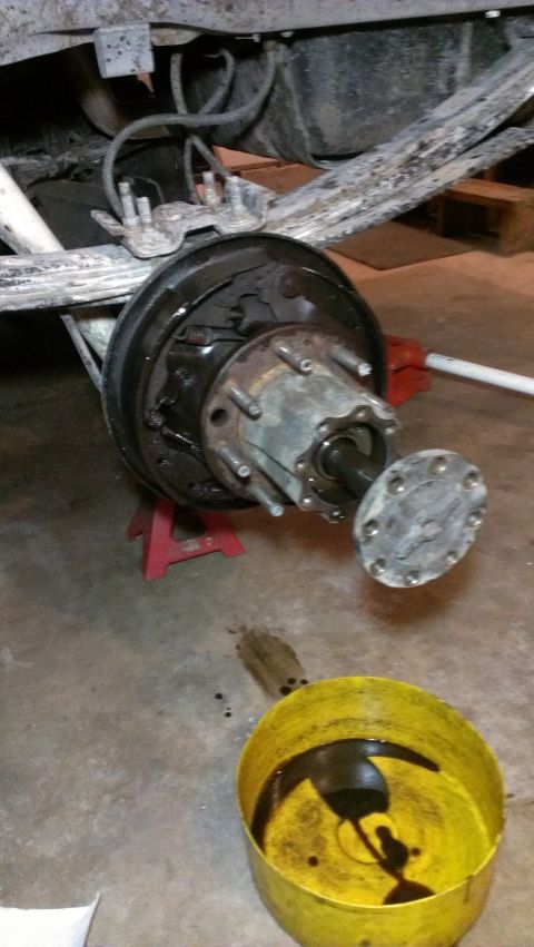 1995 Ford Bronco - Close-up of a vehicle's rear axle assembly, with the brake drum off and fluid draining into a yellow bucket.