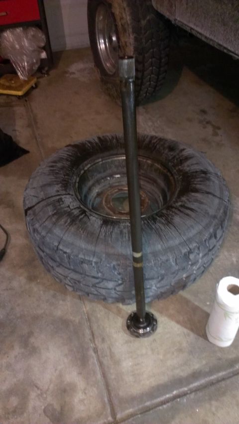 1995 Ford Bronco - An axle shaft is shown resting on a tire, with a partial view of a vehicle in the background.