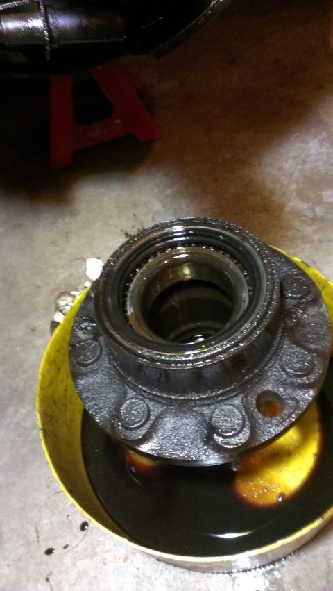 1995 Ford Bronco - A wheel hub assembly sits in a yellow bucket filled with dark oil, with a red jack stand visible in the background.