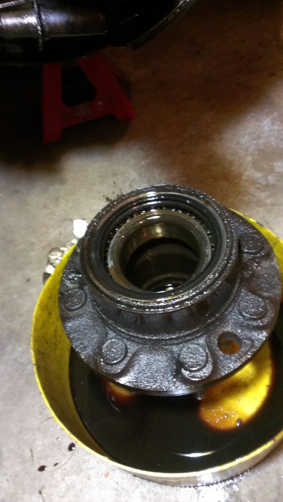 Wheel hub assembly with bolts submerged in dark oil within a yellow bucket