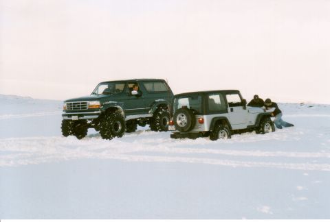1996 Ford Bronco - Two off-road vehicles are stuck in the snow, with people attempting to free one of them.