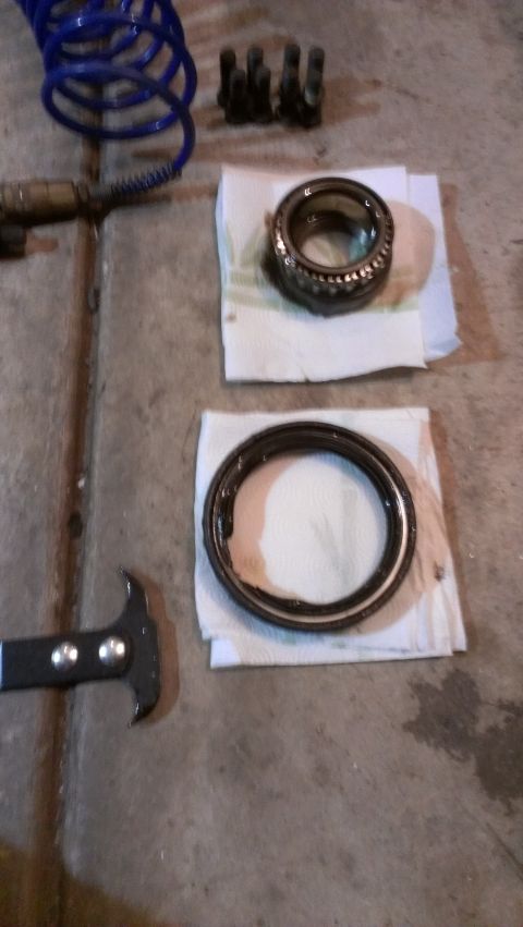1995 Ford Bronco - Wheel bearings and a seal puller are laid out on a concrete surface, likely for automotive maintenance.