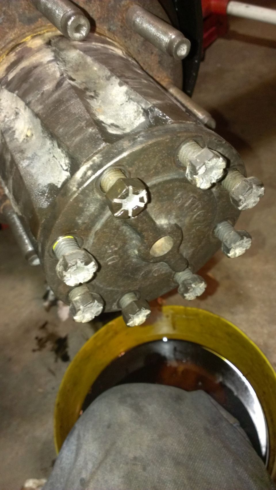 Wheel hub assembly with six lug nuts, some with white residue, over a yellow oil drain pan