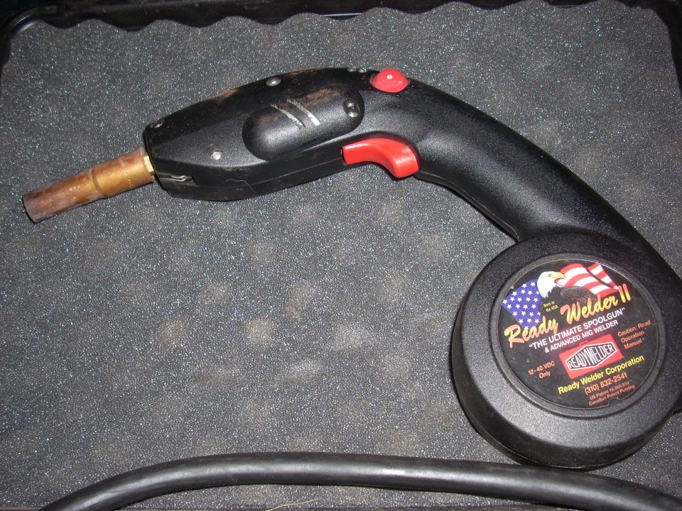 Black welding gun with red trigger and button, on a textured surface