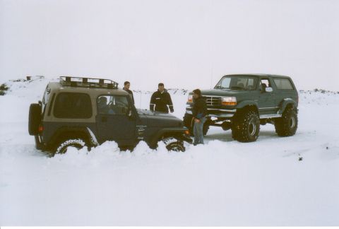 1996 Ford Bronco - A green Ford Bronco is stuck in the snow, with a Jeep partially buried beside it.