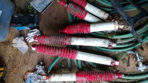 1994 Ford Bronco - Several shock absorbers are laid out on the ground, with a green garden hose coiled nearby.