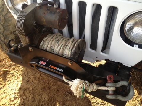 2000 Jeep TJ - Front view of a 2000 Jeep TJ showing the mounted winch and tow rope, with a portion of the grille and headlight visible.
