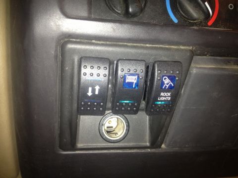 2000 Jeep TJ - Close-up of auxiliary switches and a 12V power outlet in a vehicle's dashboard.