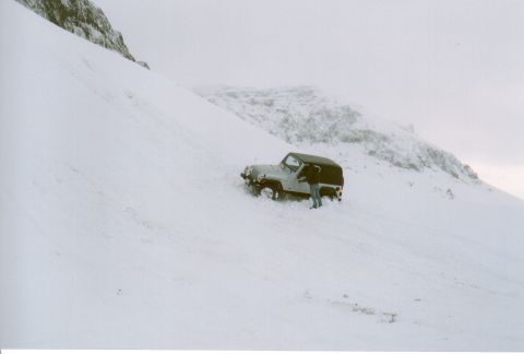 1996 Ford Bronco - A person stands next to a Jeep Wrangler that appears stuck in a snowy, mountainous area.