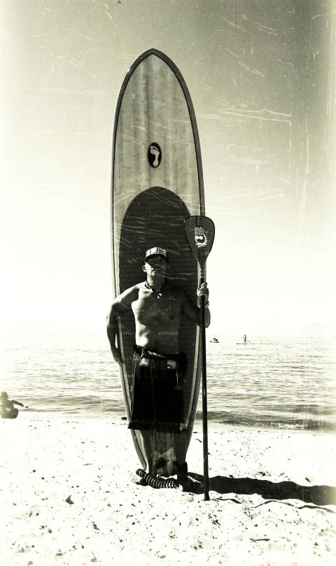 1996 Ford Bronco - A man stands on the beach with a paddleboard and paddle, ready for the water.