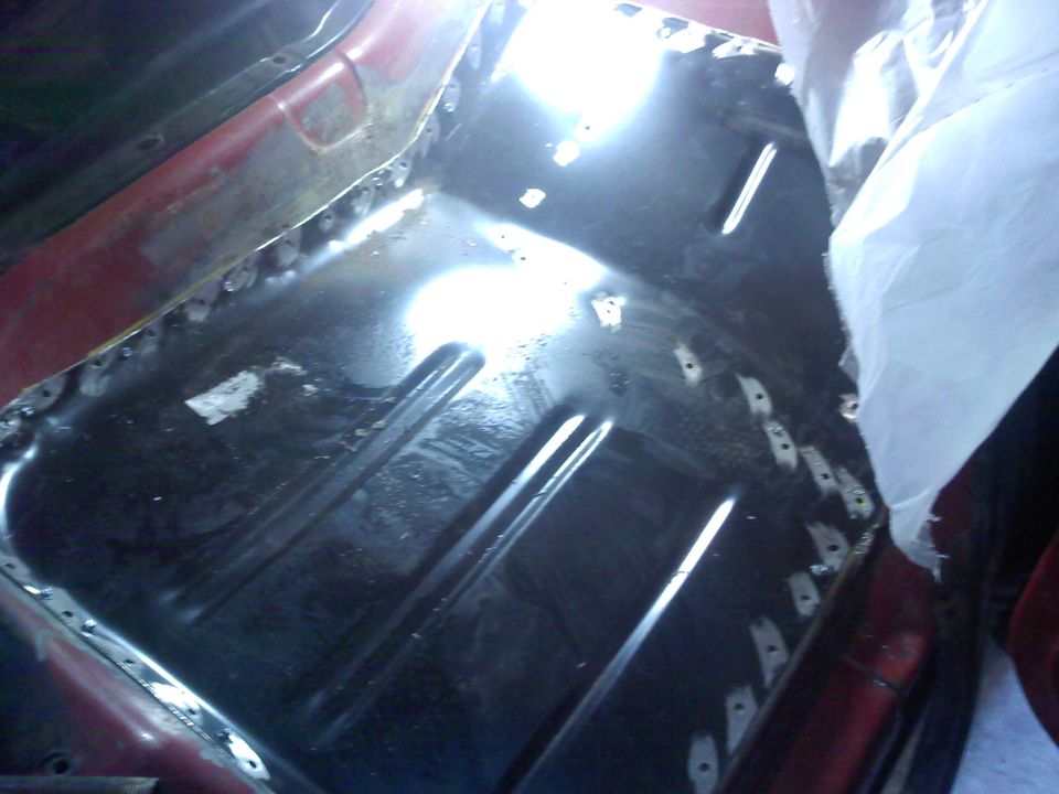 Close-up of a vehicle's floor pan undergoing repair with visible welds and a new metal patch