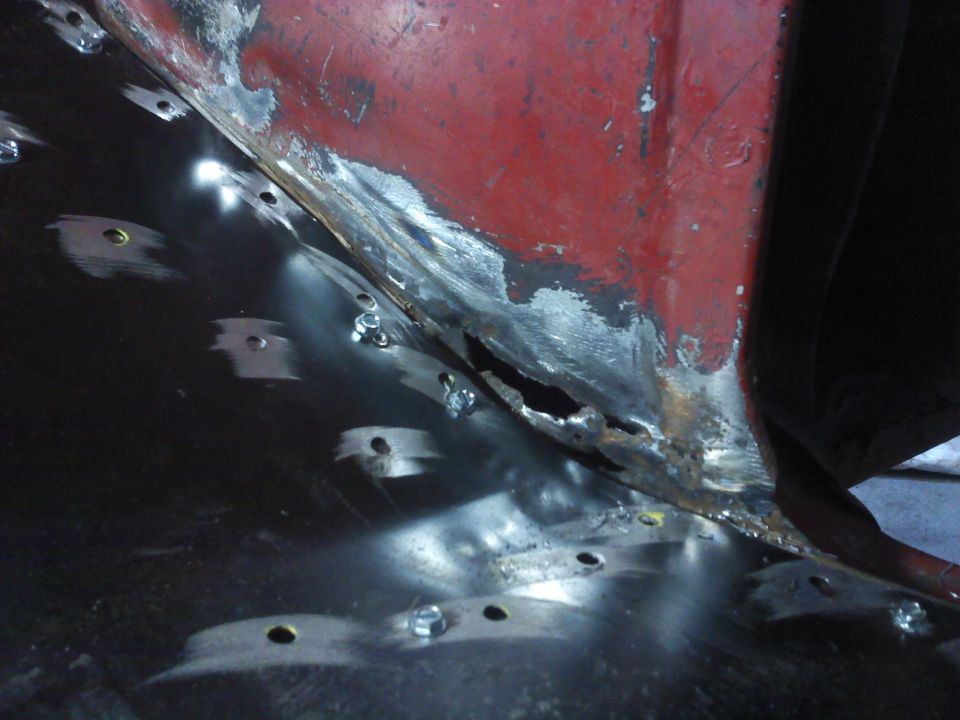 Close-up of a rusted-out vehicle floor pan being repaired with new metal and bolts