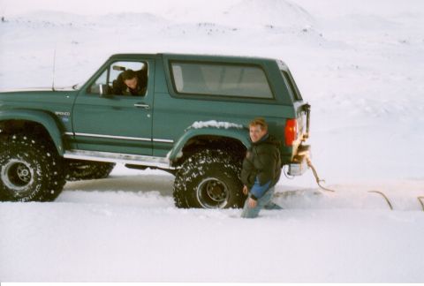1996 Ford Bronco - A green Ford Bronco is stuck in a snowy landscape with two people nearby.