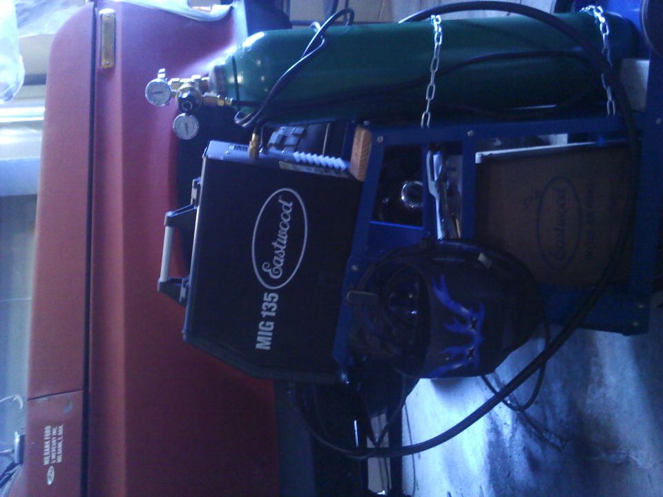Welding machine and gas tank on a cart next to a red vehicle door