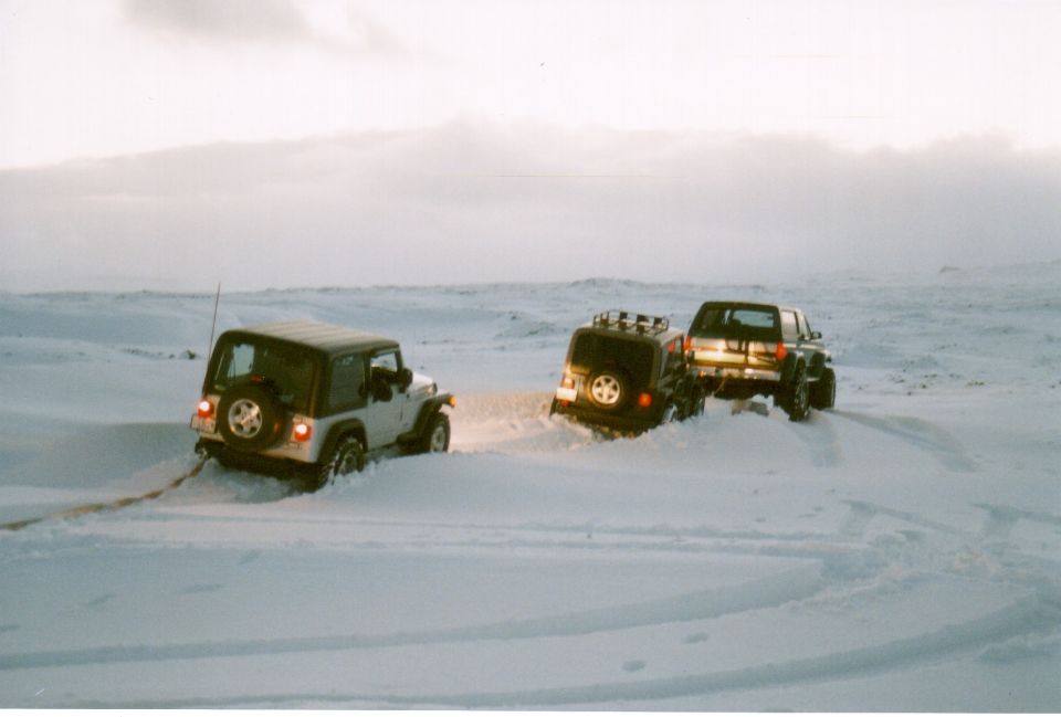 Silver Jeep, dark SUV, and lifted pickup stuck in deep snow at dusk