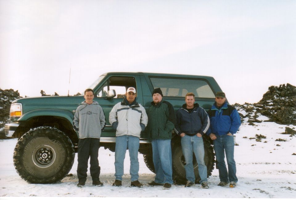 Five men posing in front of a lifted green Ford Bronco in snow