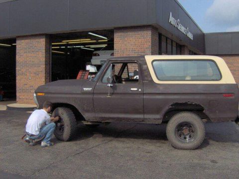 1979 Ford Bronco - A person works on the front tire of a brown 1978 Ford Bronco outside an auto service center.