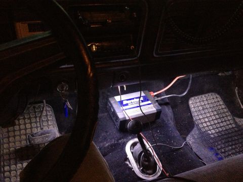 1979 Ford Bronco - The interior of a vehicle shows an aftermarket inverter installed on the floor, with visible wiring and floor mats.