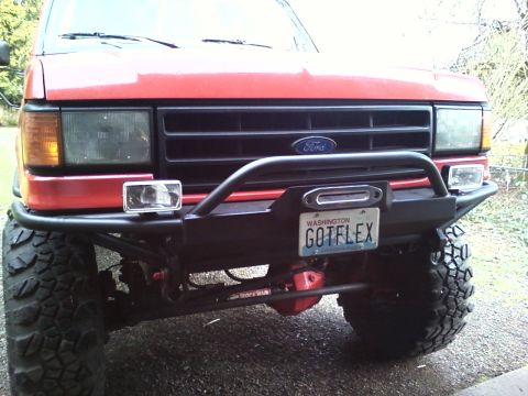 1989 Ford Bronco - Frontal view of a red Ford truck with a custom bumper and winch, fitted with large off-road tires.