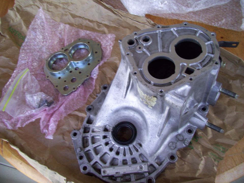 Transmission housing and adapter plate laid out on brown paper. Some small parts are in a plastic bag