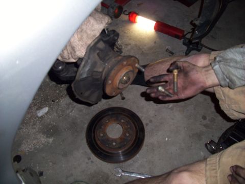 1995 Ford Probe - A mechanic works on a car's brake rotor and hub assembly, holding bolts in a dirty hand.