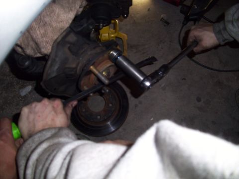 1995 Ford Probe - Mechanic working on a car's brake rotor and caliper assembly with tools.