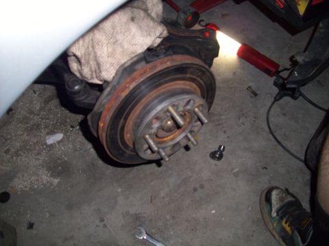 1995 Ford Probe - Close-up of a car's brake rotor and hub assembly, with tools nearby on the garage floor.