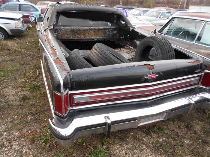 Rear-side view of a rusted black pickup truck with spare tires in the bed.