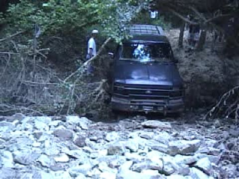 1983 Ford Bronco - A dark SUV navigates a rocky, wooded terrain.