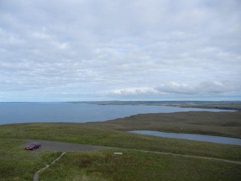 2003 Mercury Marauder - A lone red sedan is parked on a road overlooking a vast expanse of water and grassy terrain under a cloudy sky.