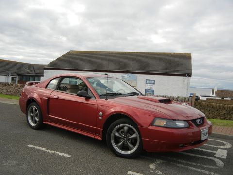 2003 Mercury Marauder - Red coupe with hood scoop parked on a street with a building in the background.