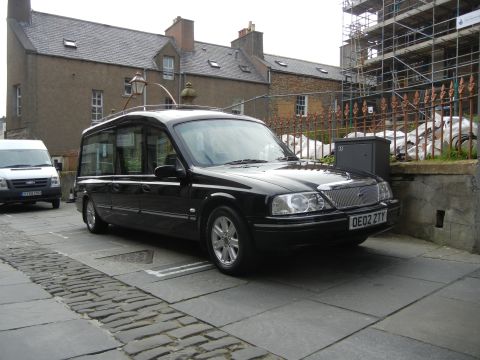 2003 Mercury Marauder - Hearse parked on a street with a white van nearby. Construction scaffolding is visible.