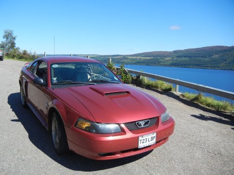 2003 Mercury Marauder - A red Ford Mustang is parked on a road overlooking a large body of water on a sunny day.
