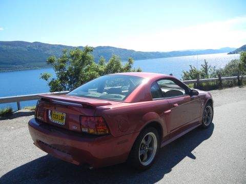 2003 Mercury Marauder - A red coupe with a spoiler and GT badge is parked by a scenic lake.