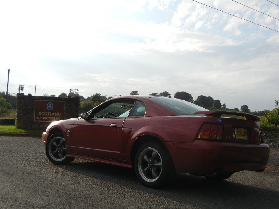 Red coupe parked near Scotland welcome sign