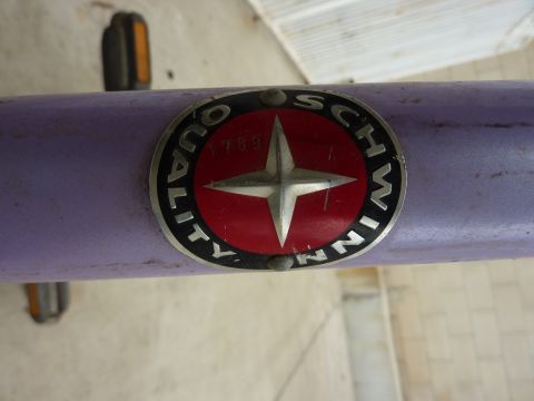 1900 Yugo GVX - A close-up view of a purple bicycle frame displaying the Schwinn Quality emblem and pedals.