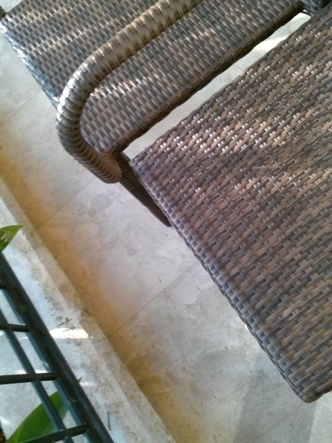 1960 Ford Falcon - Close-up of outdoor wicker furniture on a tiled patio, with a metal railing in the foreground.