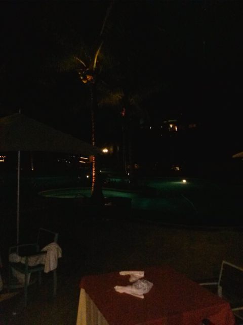 1960 Ford Falcon - A nighttime view of a resort area with a pool and palm trees, with tables and chairs in the foreground.