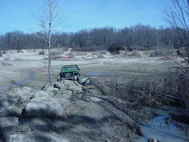 Green off-road vehicle with an orange flag on the back, navigating a rocky terrain