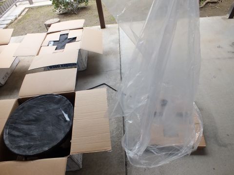 2003 Ford Crown Victoria - black round wheel piece rests in an open box next to a tall plastic-wrapped item on a patio.