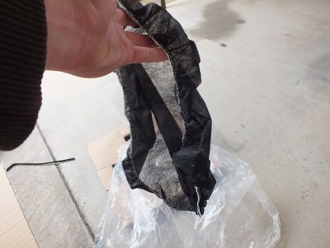 2003 Ford Crown Victoria - Black mesh protective sleeve removed from a wheel and held above a garage concrete floor