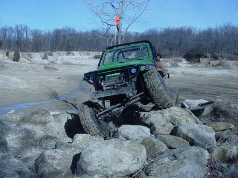 1992 Ford Bronco - A green off-road vehicle navigates a rocky terrain with a driver visible.
