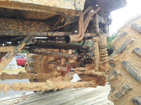 1986 Ford Bronco - Undercarriage of a heavily mud-caked vehicle, showing exhaust pipes and a massive tire. The SuperMotors logo is visible at the bottom right.