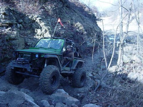1992 Ford Bronco - An off-road vehicle navigates a challenging rocky terrain on a wooded hillside.