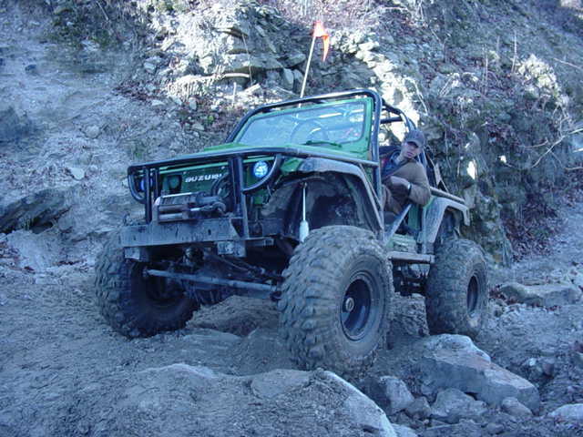Green off-road vehicle with large tires on rocky terrain